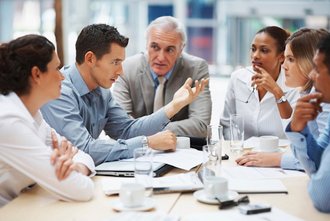 Erwachsene Personen sitzen beim Geschäftstermin gemeinsam am Besprechungstisch.